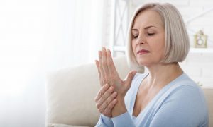featured-early-signs-of-arthritis-joint-pain-vs-ageing | Aaria Rheumatology Woman stretching her stiff fingers in the morning — early arthritis awareness.