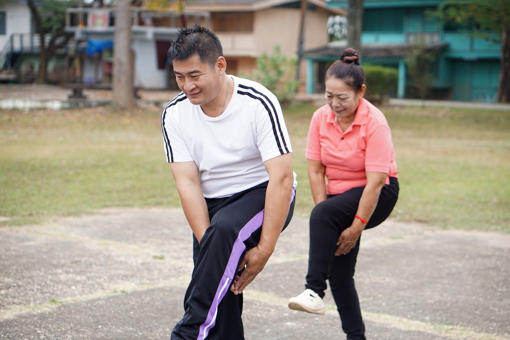 Active Asian senior couple stretching legs together in a park