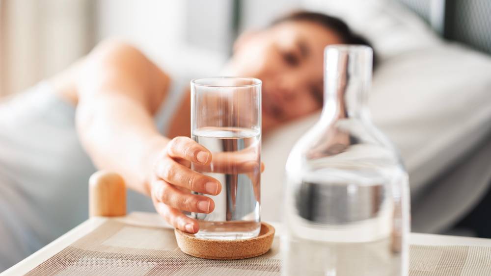 Woman reaching for a glass in bed.
